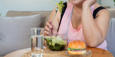 Mindful overweight woman choosing a healthy salad over a tempting burger, focusing on her weight...