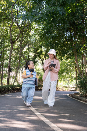 Diverse friends walking and chatting in a serene park, enjoying technology and nature togetherの写真素材