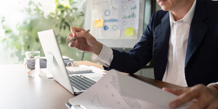 Elderly businessman discussing data insights while reviewing reports in a modern officeの写真素材