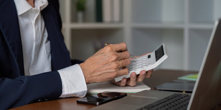 Senior financial consultant using calculator and reviewing notes in a stylish office workspace