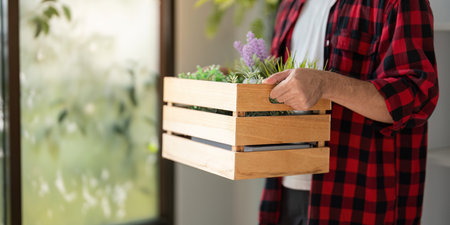 Young man holding a wooden crate filled with vibrant indoor plants, showcasing his passion for gardeningの写真素材