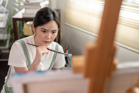 young artist contemplating her painting in bright studio showcasing dedication and creativityの写真素材