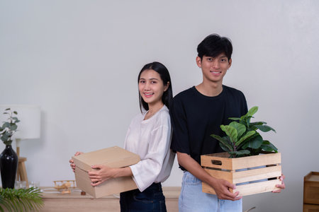 Cheerful couple posing with moving boxes and plants in their new home, celebrating a fresh start