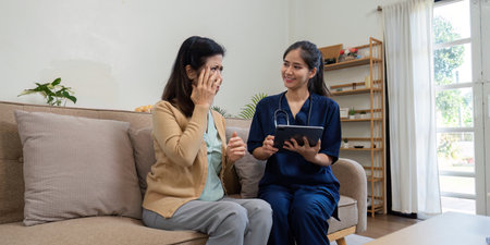 Caregiver using tablet to discuss health concerns with elderly patient, focusing on disease symptoms and careの写真素材