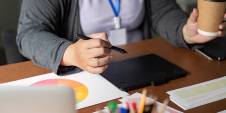 Graphic designer sketching ideas and holding a coffee cup in a modern workspace, showcasing...