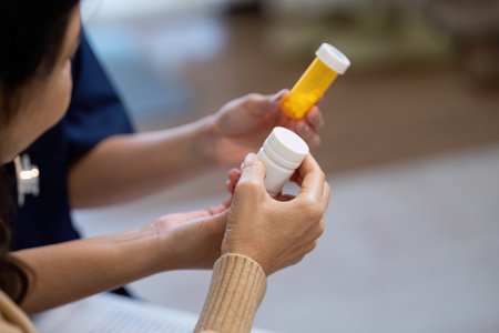 Elderly patient discussing symptoms with caregiver while holding medication bottlesの写真素材