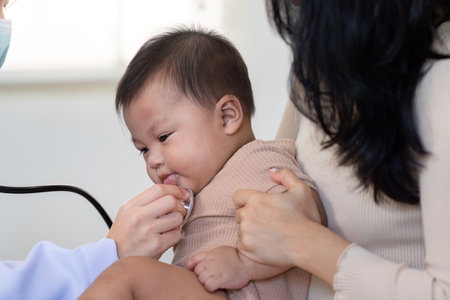 Pediatrician using stethoscope on baby during a checkup with attentive motherの写真素材