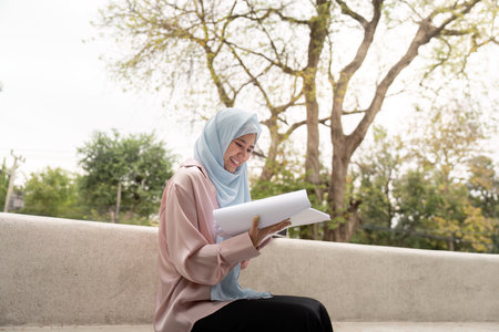 Muslim woman reviewing business documents in a serene outdoor setting.の写真素材
