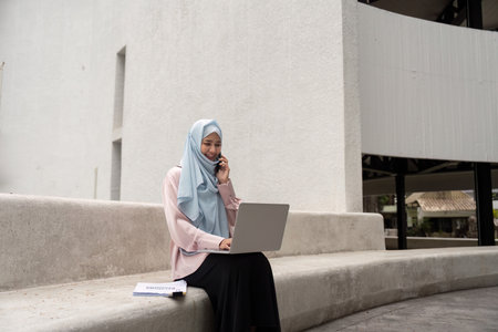 Muslim woman in hijab on a business call while working on her laptopの写真素材