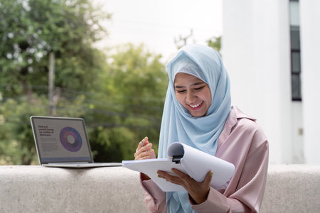 Muslim business woman in hijab reviewing documents and smiling outdoors.の写真素材