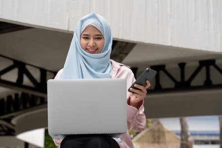 Muslim woman in hijab working on laptop and smartphone for business successの写真素材