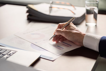 Elderly businessman analyzing financial reports and charts while taking notes at a modern office...