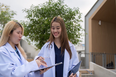 Diverse female doctors collaborating on patient notes outside a medical facility.の写真素材