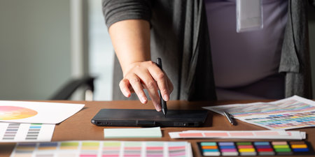 Graphic designer using a digital tablet to create designs at a wooden workspace.