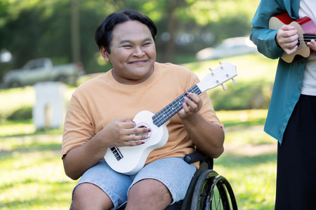 Young man in a wheelchair happily playing ukulele in a sunny park.の写真素材