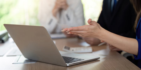Close-up of hands discussing financial data over a laptop in a collaborative meeting environment.