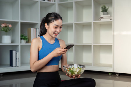 Woman sitting cross legged with a bowl of healthy salad and smartphone in a modern living space.の写真素材
