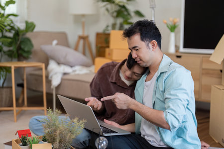LGBTQ couple working on a laptop while unpacking in their new home.の写真素材