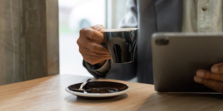 Elderly man holding a coffee cup and using a tablet in a cafe, reflecting on business matters.