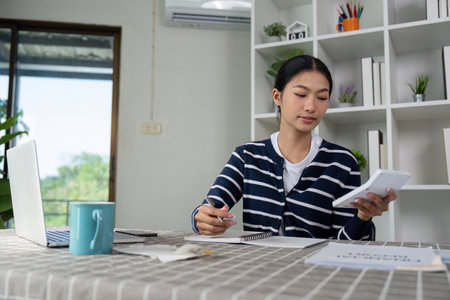 Young woman managing finances with calculator and bills on a tableの写真素材