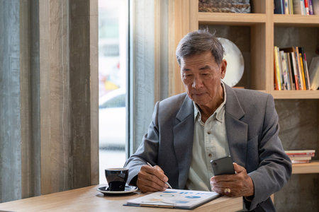 Senior businessman analyzing documents on a tablet while sipping coffee in a contemporary cafe.の写真素材