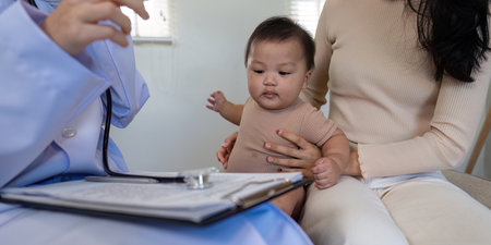 Pediatric doctor discussing baby health report with parent while holding child in clinic.の写真素材