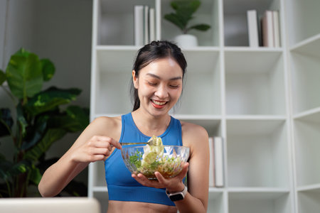 Woman enjoying a healthy salad while smiling at a laptop, promoting wellness and healthy eating habits.の写真素材