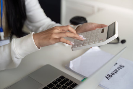 Financial analyst calculating tax refund and deductions using a calculator at a desk.