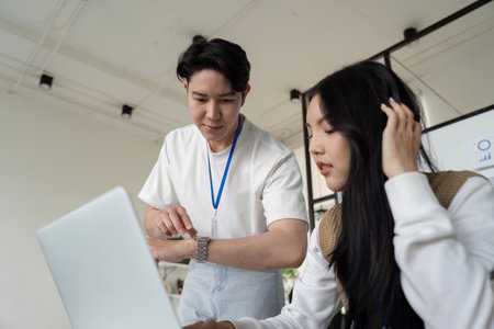 Financial team member checking time while collaborating on a laptop with a colleague.の写真素材