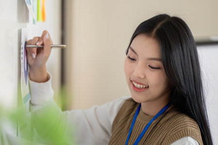 Young professional analyzing data on a board, showcasing teamwork and strategic planning in a modern...