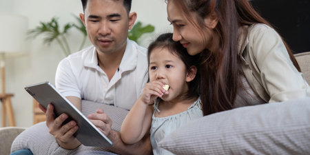 Family sharing a tablet while enjoying snacks and bonding together.の写真素材