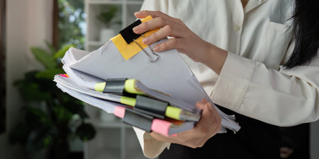Individual reviewing tax documents with a magnifying glass while seated at a desk.