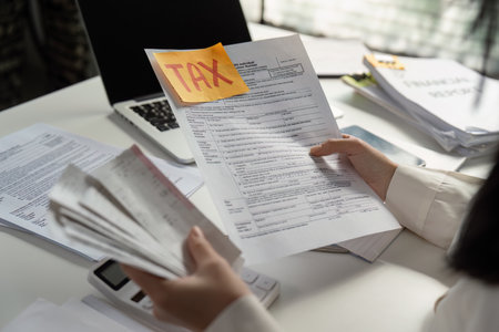 Person analyzing tax paperwork and using a calculator for financial calculations.の写真素材
