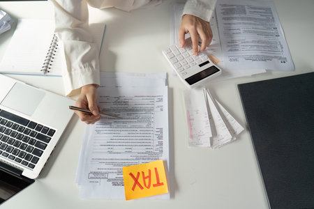 Young woman calculating taxes and preparing financial documents at a desk with a calculator.