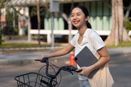 Smiling woman walking with bicycle and tablet, embracing sustainable living.の写真素材
