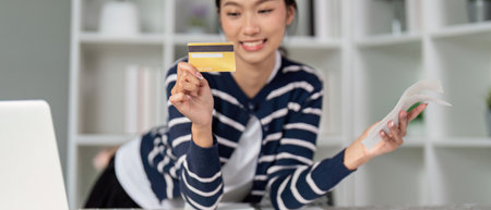 Happy woman holding a credit card and bill, celebrating financial success.の写真素材
