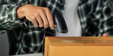 Close-up of a young man scanning a package with a barcode scanner in a workspace.の写真素材