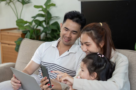 Happy family sharing moments on the couch with devices and laughterの写真素材