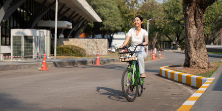 Happy woman riding a green bicycle in a sunny urban environment, promoting sustainability.の写真素材