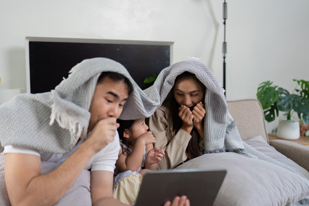 Cozy Family Moments and Screen Time. A family watches a film under a shared blanket, sharing laughs and popcorn.の写真素材