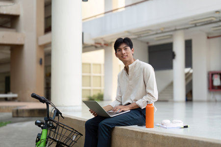 Digital Work and Sustainability. A young man with a laptop sits beside his bicycle, engaged in...