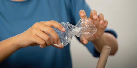 Hands-on Recycling Practices. A child learns how to crush plastic waste to prepare it for recycling,...