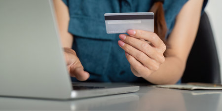 Digital Payments and Credit Management. Close-up of a hand holding a credit card over a laptop, reflecting modern finance solutions.の写真素材