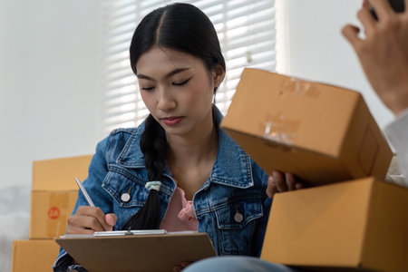 Planning and Organization in E-Commerce. A young entrepreneur jotting down notes while managing product inventory.の写真素材