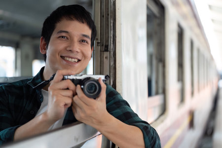 Adventure and Creativity. A cheerful traveler poses with his camera at the train window.の写真素材