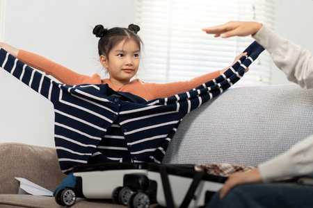 Fun Packing and Adventure. A little girl joyfully tries on clothes while helping with packing for a family trip.の写真素材