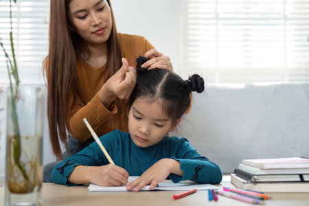 Bonding Through Education and Grooming. A parent helps a child with hair while she focuses on her...