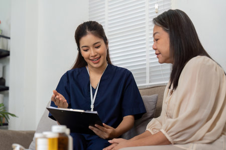 Caregiver Support and Health Consultation. A compassionate caregiver discusses medication with a patient during a home visit.の写真素材
