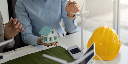Sustainable Development and ESG Practices. A team discussing eco-friendly construction using a model house and wind turbines.の写真素材