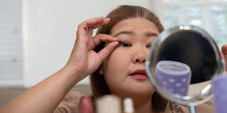 Eye Makeup and Precision. A woman applying false eyelashes while looking in the mirror, focusing on...